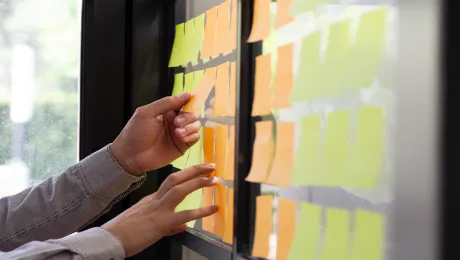 Yellow and orange post it notes being applied to a wall by a person