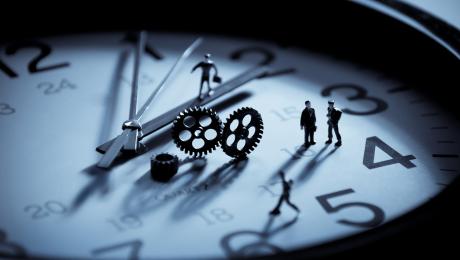 Face of a clock with tiny people standing on it.